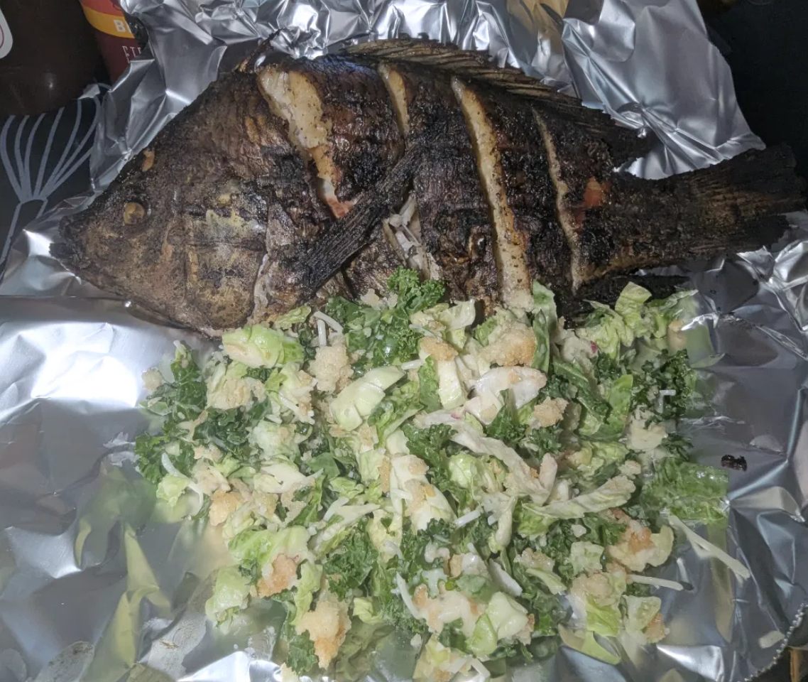 A whole charred tilapia, scored and grilled, served with a fresh green salad