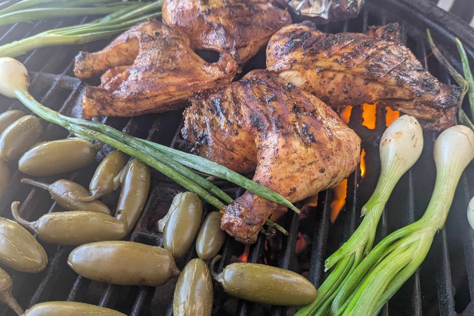 Chicken quarters, jalapeños and cebollitas over open flame on a kamado grill, with a foil packet of tortillas warming in the corner.