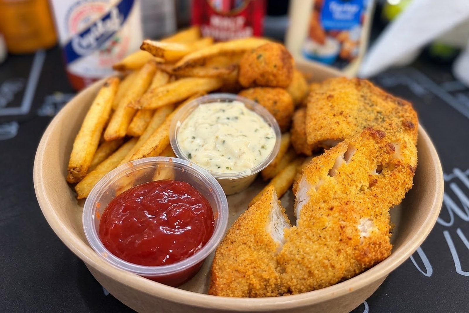 A fried catfish fillet cut open on a plate with fries, hush puppies, ketchup and tartar sauce